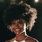 A beautiful woman with afro hair smiling outdoors at night under soft lights.